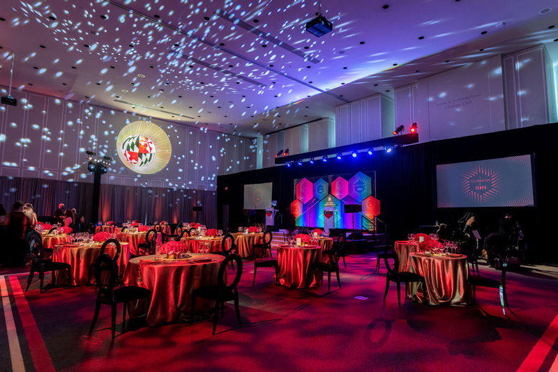 The Dorothy D. & Nicholas Orem Alumni Hall at the Samual Riggs IV Alumni Center, decorated for A Celebration of Terps with spaced out tables, crystal ball lighting, and a stage for presentations